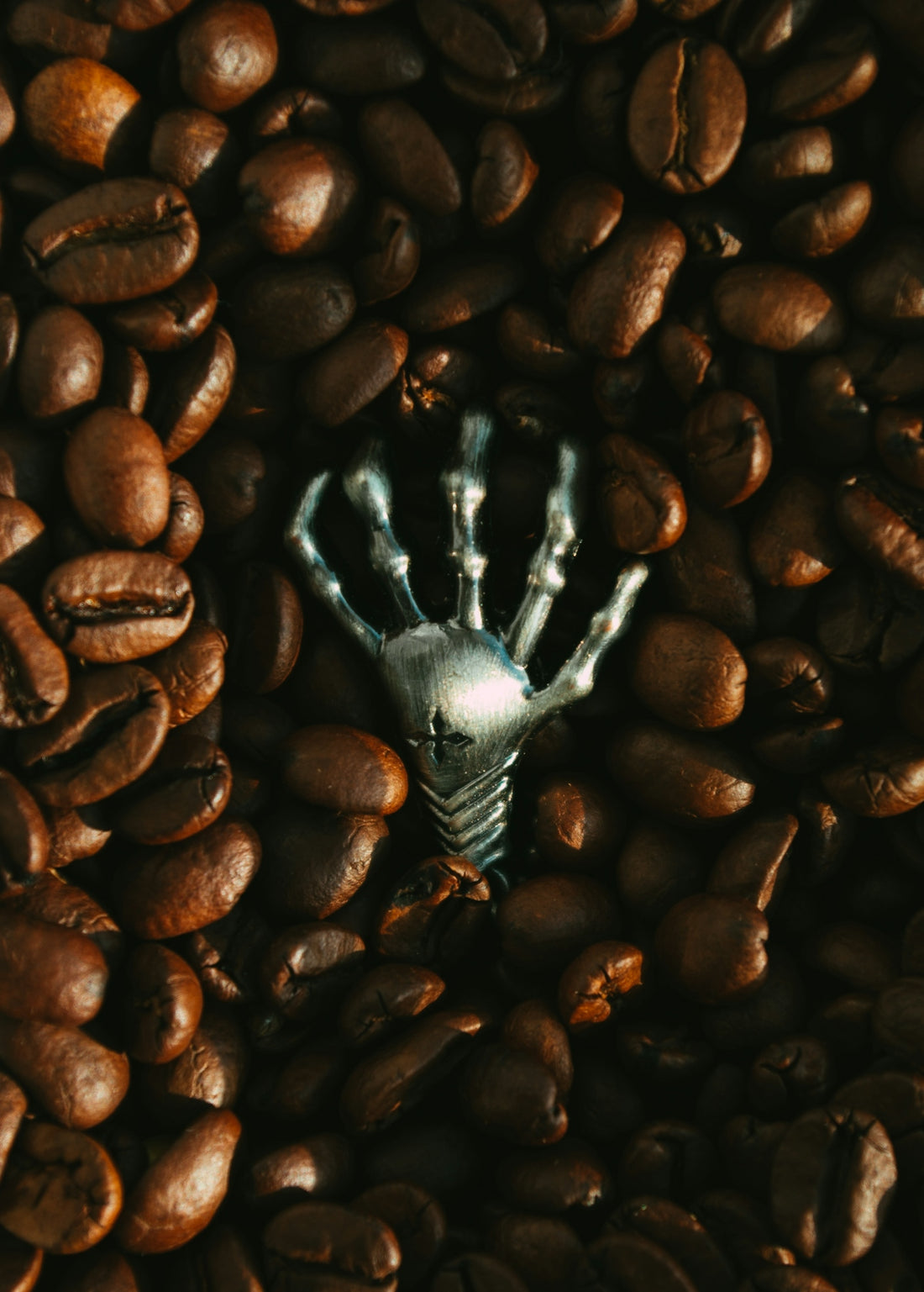 a picture of a skeleton hand in a pile of coffee beans