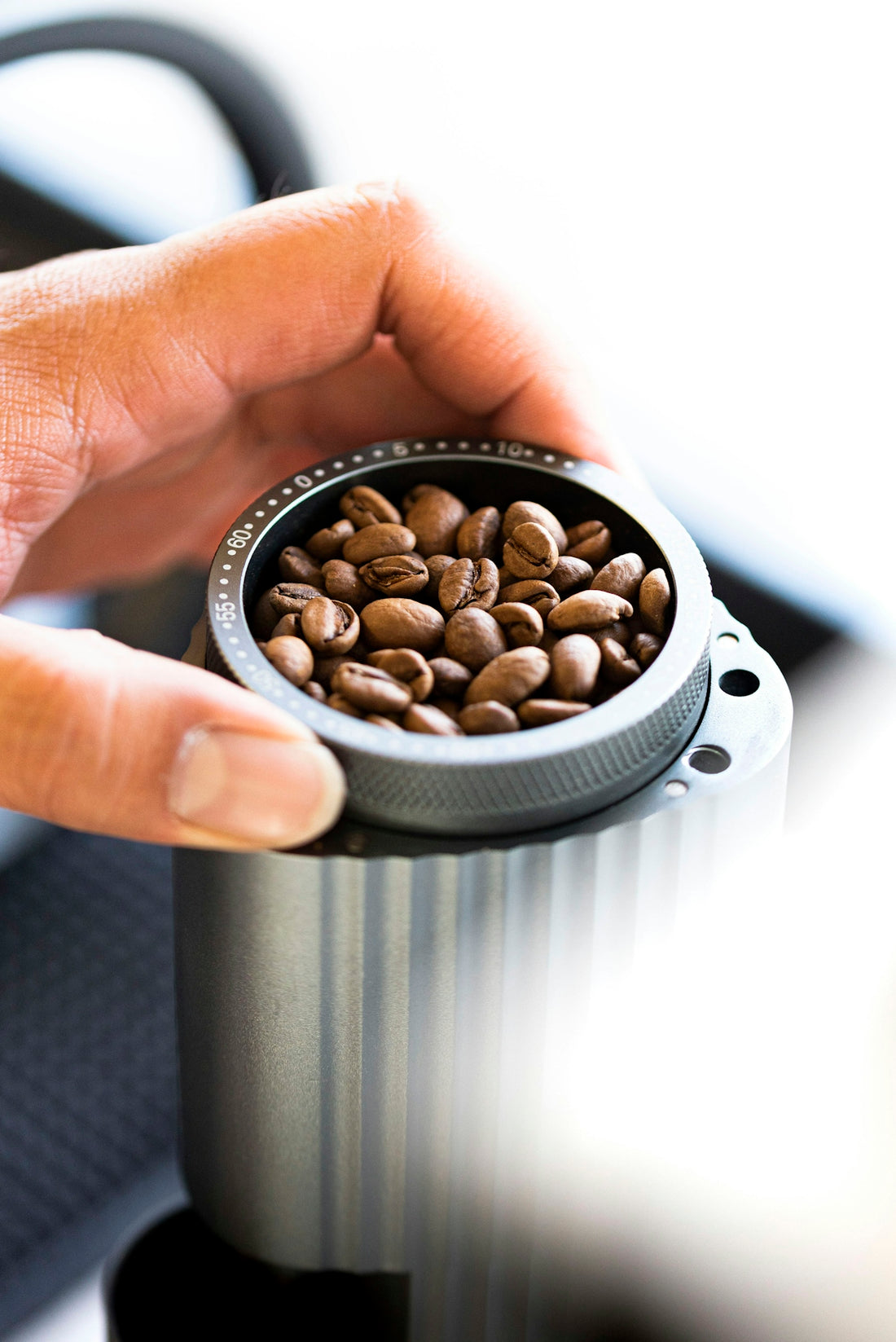 A person is holding a coffee grinder with coffee beans in it